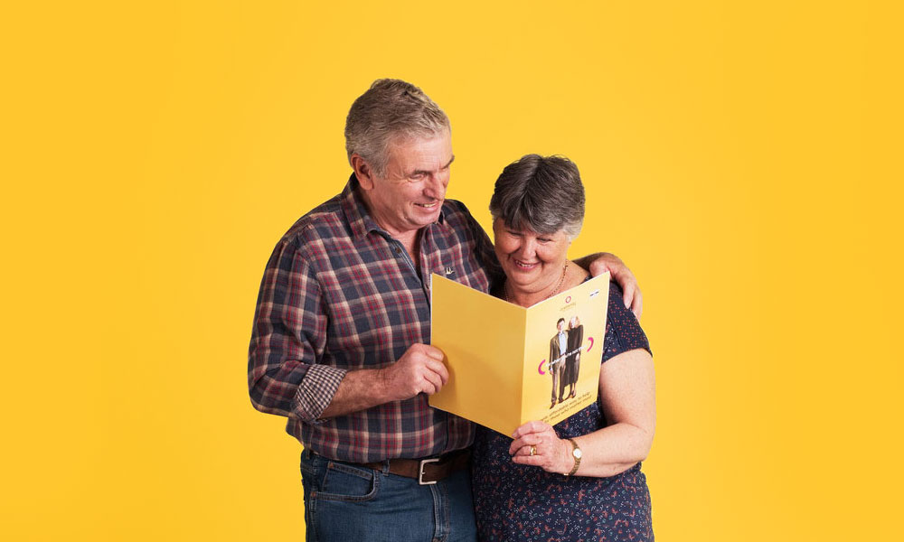 A man and a woman standing together, reading through a OneFamily Over 50s life cover brochure